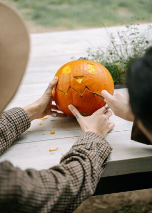 Two people carving a jack-o'-lantern on a wooden table outdoors during fall.