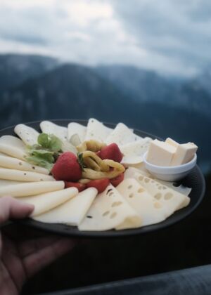 A person holding a plate of cheese and fruit